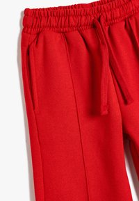 Pantalones de chándal rojos hechos de una tela suave, con una cintura elástica y cordón, bolsillos laterales y un diseño de pierna recta.