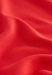 Red ribbed fabric featuring a smooth texture with subtle lines, showcasing undulating folds and depth in color.