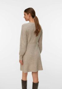 Beige strikket kjole med lange ærmer, ribbet tekstur, tætsiddende talje, flagrende kant og rund halsudskæring. Accepteret med brune knæhøje støvler.