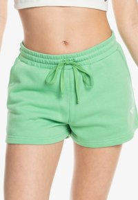 Shorts verts en mélange de coton avec une taille élastique et un cordon de serrage. Ils présentent une texture lisse et un petit logo en accent sur l'ourlet.
