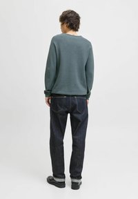 Jeansi din denim de un albastru închis, asortați cu un pulover gri, având o croială lejeră, manșete cu șnur și detalii vizibile de cusătură. Pantofii negri completează lookul.