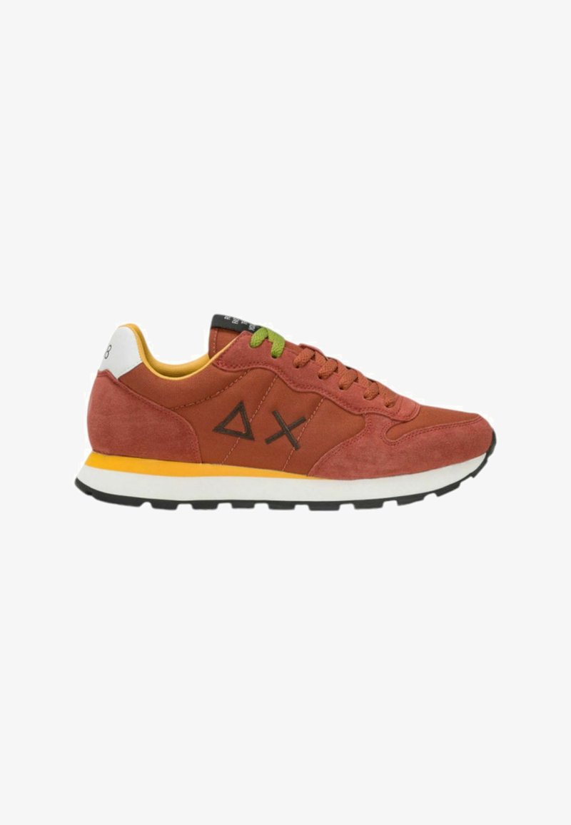Sneaker rossa in suede con accenti geometrici neri, suola gialla e lacci verdi, dotata di un tallone bianco e colletto alla caviglia imbottito.