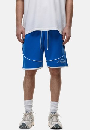 Shorts de sport bleu avec des accents et des bordures blanches. Équipés d'une taille élastique avec cordon de serrage. Associés à des baskets claires et des chaussettes blanches.