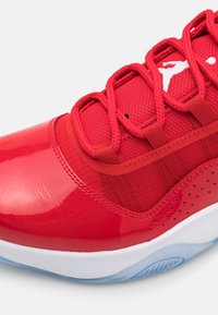 Chaussure de sport rouge avec une tige en cuir verni brillant, des accents en mesh texturé et une semelle bleu glacé. Les lacets sont tissés pour un maintien sécurisé.