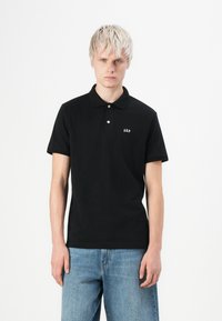 Polo noir en coton avec un col et des manches courtes, arborant un petit logo blanc "GAP" sur la poitrine gauche.