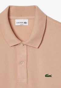 Vaalean persikan värinen poolopaita, jossa on teksturoitu kangas, slim fit -kuosi, kaksi nappia ja vihreä brodeerattu krokotiililogo vasemmassa rinnassa.