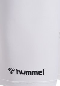 Vita träningsshorts i vitt tyg med en slät yta, försedda med en liten svart logotyp med en bi-design nära nederkanten och diskreta sömdetaljer.