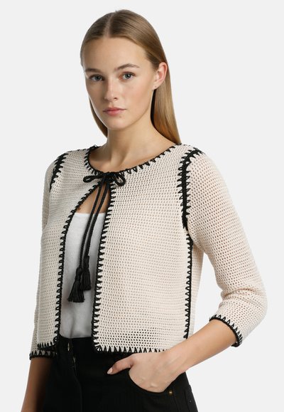 Virkat cardigan i off-white med svart kant och fransband, med trekvartslånga ärmar och en fyrkantig passform.
