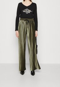 Černý dlouhý rukáv top s V-výstřihem a ozdobným designem z kamínků, spojený s širokými plisovanými kalhotami z olivově zeleného sametu.