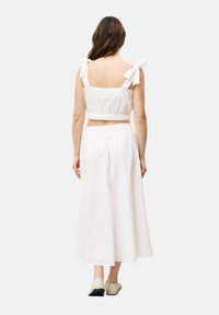 Weißes Baumwoll-Crop-Top mit Bindebändern, kombiniert mit einem luftigen Rock. Strukturierter Stoff mit dezenten Stickereien, lockere Passform und elastischer Bund.