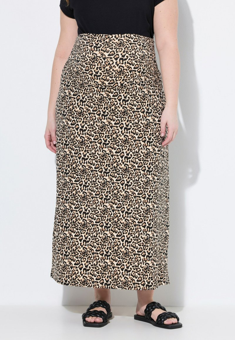 Falda maxi de estampado de leopardo con cintura alta, confeccionada en una tela suave, combinada con una blusa negra y sandalias planas con tiras trenzadas.