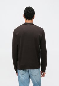 Camicia marrone a maniche lunghe con una texture a coste e un taglio dritto. Presenta un colletto classico ed è abbinata a jeans di denim azzurro chiaro.