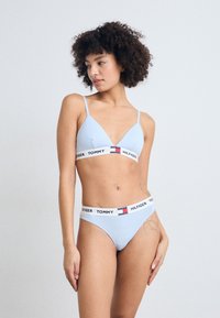 Lys blå bikini-sett med trekantformet bh med tynne stropper og logoet elastisk bånd, sammen med matchende lavtsittere thong. Glatt tekstur av stoff.