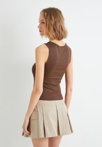 Top de tirantes marrón con canalé y escote redondo, combinado con una falda de pliegues beige que cuenta con bolsillos laterales. La parte superior se ajusta ceñidamente, enfatizando una silueta estilizada.
