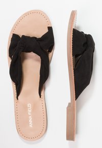 Black suede slide sandals featuring a knotted upper, a tan leather insole, and a flat rubber outsole with stitching details.