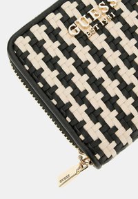 Portefeuille tissé avec un motif noir et beige, présentant un logo doré, des bords en cuir et un zip doré avec un détail de marque.