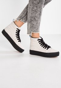 Hochschuhe aus hellgrauem Wildleder mit schwarzen Schnürsenkeln und Gummisohle. Mit einer hinteren Schlaufe und strukturierter schwarzer Laufsohle. Zeigt ausgefranste Jeans.