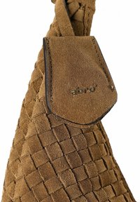 Sac à main en daim couleur tan avec une texture tissée et une étiquette en cuir lisse marron portant le logo "abro" en lettres métalliques.