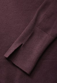Pull en maille bourgogne avec des poignets et un ourlet côtelés, et un détail fendu sur le côté ; texture lisse et couleur uniforme.