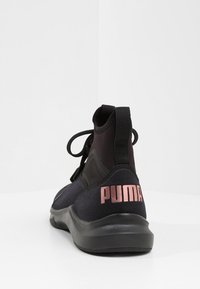 Svart träningsskor med hög klackdesign, tillverkade av mesh och syntetiska material, med en rosa logotyp på hälen och en texturerad sula.