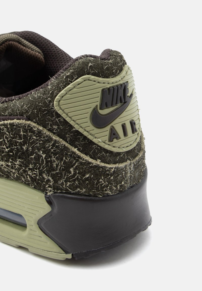 Dark green sneaker with textured fabric upper, plastic accents, and visible Nike logo. Features a rounded heel and cushioned sole.