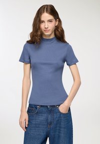Prążkowany top z krótkim rękawem w miękkim odcieniu niebieskiego z golfem. Dopasowany krój podkreśla sylwetkę. Połączony z dżinsami w ciemnoniebieskim kolorze o wysokim stanie.
