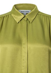 Grüne Satinbluse mit Kragen, Frontknopfverschluss und Falten an den Schultern. Markenetikett: MORE & MORE. Größe: 36.