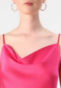 Fuchsia satengensere med tynne stropper og en bølgende utringning. Modellen har store sølvøredobber. Myk tekstur og livlig farge.