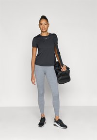 Μαύρο κοντομάνικο μπλουζάκι Nike, γκρι κολάν, μαύρα αθλητικά παπούτσια και μαύρη τσάντα ώμου. Λείο ύφασμα, εφαρμοστό σχέδιο, ελάχιστα λογότυπα.