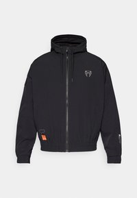 Sort zip-jakke med hætte, elastiske manchetter og snoretræk. Har et logo på brystet og et orange mærke på siden.