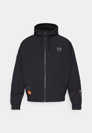 Black zip-up jacket with a hood, elastic cuffs, and a drawstring. Features a logo on the chest and an orange tag on the side.