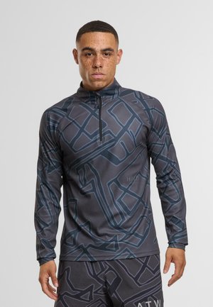 Camiseta deportiva de manga larga con cremallera en gris oscuro con un patrón geométrico azul. Presenta un cuello alto y tejido texturizado.