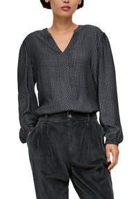 Blouse à manches longues bleu foncé avec un motif pied-de-poule, dotée d'un col en V et d'une texture douce, associée à un pantalon en velours côtelé sombre.
