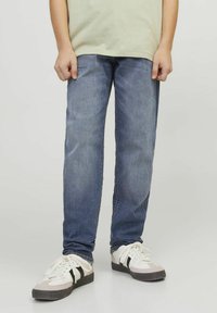 Denim jeans v srednjem modrem pranju, ravno krojenje, z diskretnim zbledelostmi. V kombinaciji z belimi supergami z črnimi akcenti in sivi detalji.