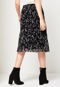 Černá plisovaná sukně s bílým květinovým vzorem, spojená s černými kotníkovými botami se zlatým zipem. Texturovaná tkanina, sukně střední délky.