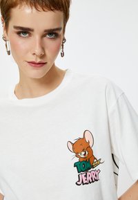 Witte katoenen t-shirt met een cartoonafbeelding van Jerry uit "Tom en Jerry" in bruine en pastelkleuren, met vette tekst. Korte mouwen.