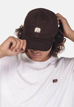Brun bomuldsbaseballcap med et broderet elefantlogo på forsiden, parret med en hvid t-shirt med rund hals, der har et lille brunt elefantdesign.