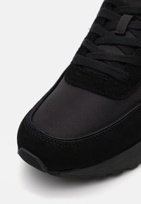 Zwarte sneaker met een combinatie van glad synthetisch materiaal en gestructureerd suede. Vetersluiting met stiksels aan de voorkant, rubberen zool.