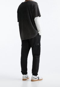 Schwarzes oversized T-Shirt mit verblasster Textur, kombiniert mit schwarzen Cargo-Hosen mit Taschen und elastischen Bündchen, und weißen Sneakers mit grauen Akzenten.