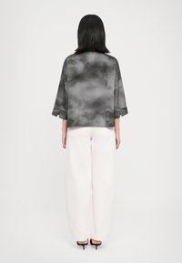 Top oversize grigio a tie-dye con maniche 3/4, abbinato a pantaloni oversize rosa chiaro e tacchi neri. Tessuto morbido e vestibilità rilassata.