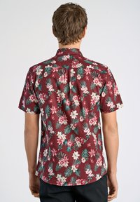 Korte mouwen shirt in bordeaux met een bloemenpatroon met witte en roze bloemen en groene bladeren. Gemaakt van lichtgewicht stof.