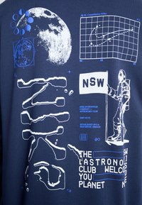 Tissu bleu marine présentant des imprimés graphiques blancs et bleus, comprenant une lune, un astronaute, une carte des constellations et du texte. Diverses formes et textures.
