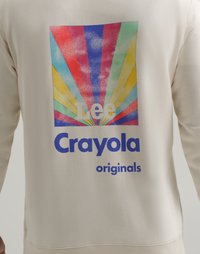 Lys beige sweatshirt med et fargerikt grafisk motiv med stråler i rødt, blått, gult og grønt, samt blå tekst som sier "Crayola originals."