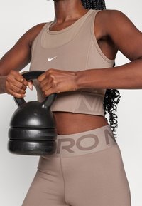 Top sportivo corto marrone con logo Nike e leggings a vita alta abbinati. Kettlebell nera tenuta saldamente, con finitura liscia e forma arrotondata.