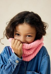 Cerniera rosa indossata con una giacca di jeans. La cerniera ha una texture a coste e la giacca presenta dettagli a scatto in metallo e una tasca.