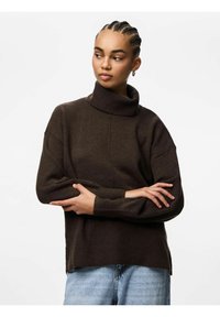 Maglione dolcevita marrone scuro in tessuto a maglia, con vestibilità comoda, polsini a coste e spacchi laterali. Abbinato a jeans azzurri chiari.