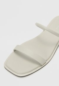 Lys grå flate sandaler med to smale stropper, firkantet tådesign, glatt matt overflate og subtil svart kant langs sålen.
