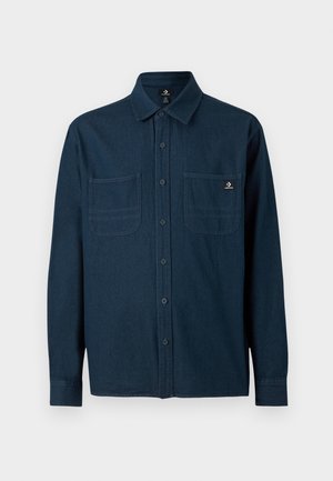 Mørkeblå skjorte med lange ærmer og knapper, med to brystlommer, hvoraf den ene har et lille Converse-logo.