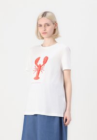 Camiseta de algodón blanca con un gráfico de una langosta roja y el texto "Solo llámame egoísta." Mangas cortas y corte holgado. Fondo liso.