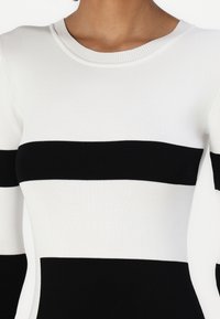 Ribbad stickad klänning med djärva svarta och vita horisontella ränder, rund halsringning och långa ärmar med kontrasterande färgavsnitt.